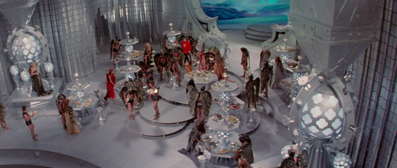 Flash Gordon (1980) movie still: wide — A futuristic grand hall features tiered metallic platforms and large glowing orb architectural elements.…