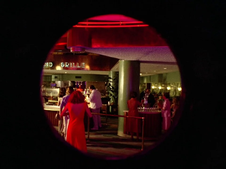 One From The Heart (1982) movie still: wide — An interior of a restaurant viewed through a dark circular porthole or lens. Patrons dressed in…