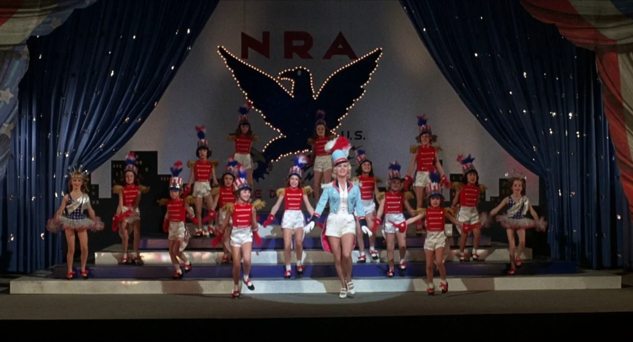What’s the Matter with Helen? (1971) movie still: wide — A decorated stage displays a large illuminated eagle emblem above a patriotic performance…