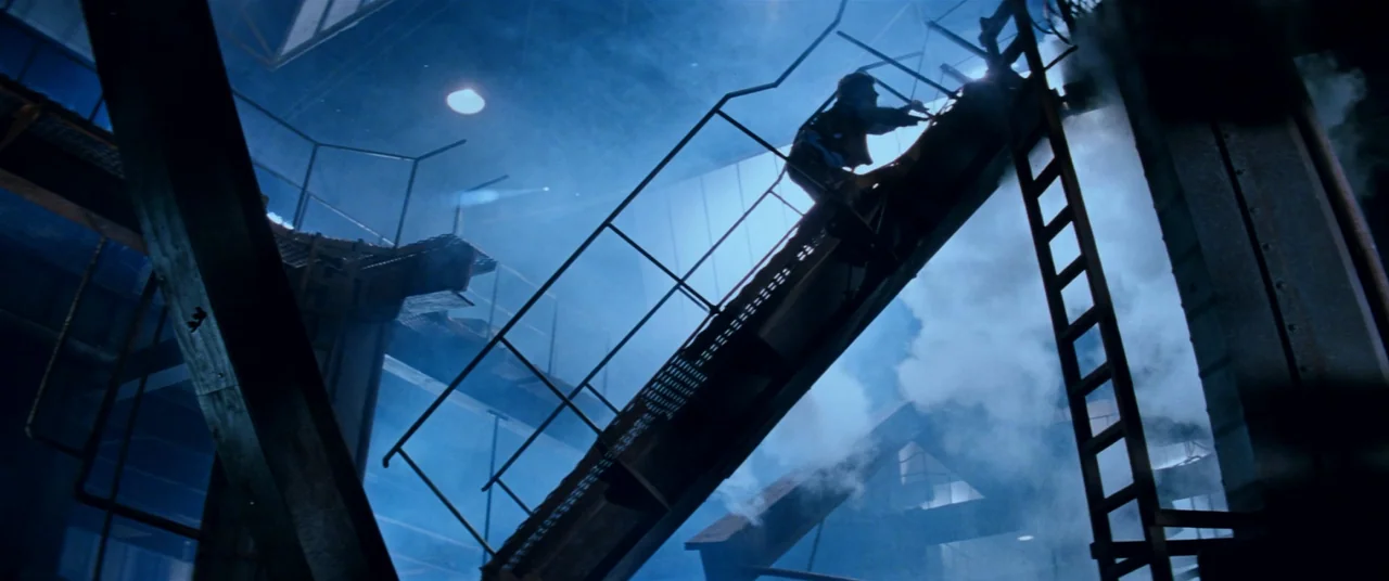 Razorback (1984) movie still: wide — An industrial facility features a steep metal staircase surrounded by dense, rising steam. A lone figure climbs…