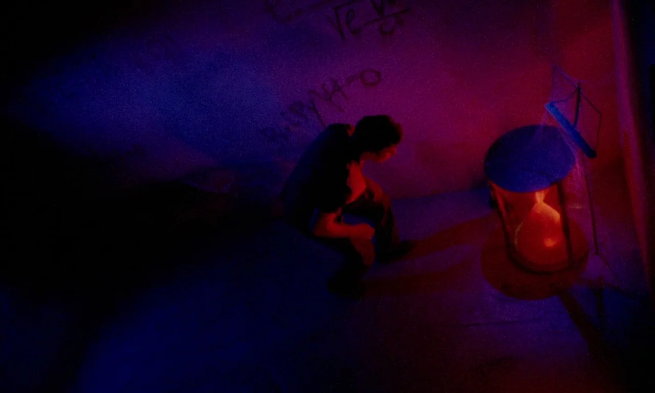 Paganini Horror (1989) movie still: wide — A dark, cramped room features concrete walls marked with faded white chalk equations. A man crouches on…