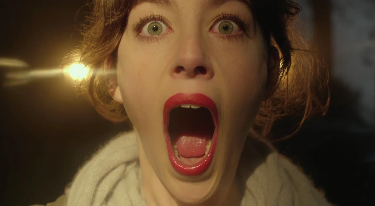 Cosmos (2015) movie still: closeup — A woman's face is centered in a dimly lit, nondescript dark environment. She stares directly into the lens with…