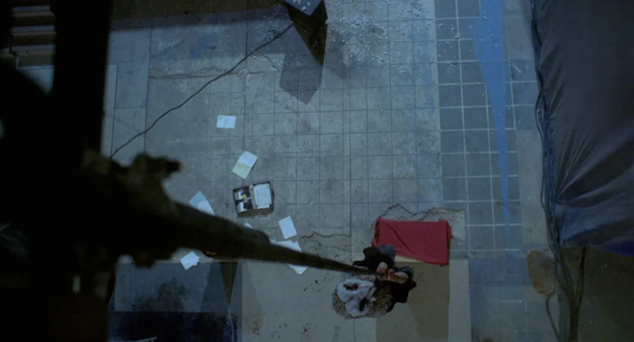 StageFright (1987) movie still: wide — An industrial space features a large tiled floor scattered with loose papers and debris. A man hangs…