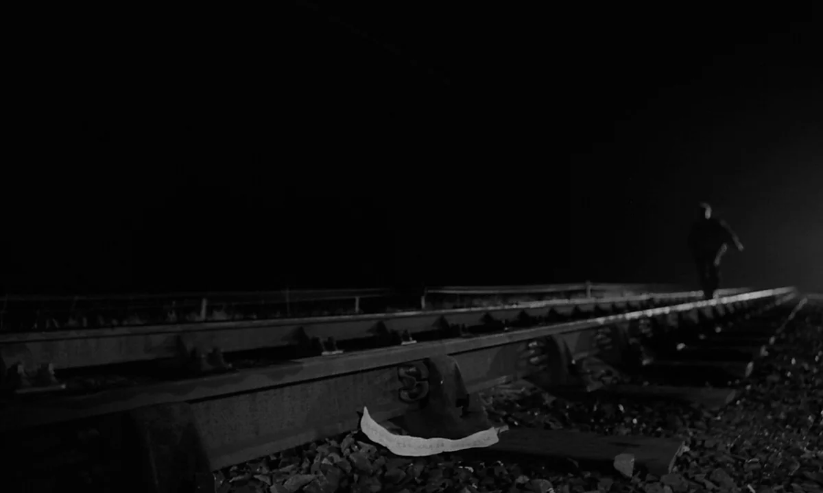 Night Of The Demon (1957) movie still: wide — A dark railway track extends into the distance under the cover of night. A lone figure walks away from…