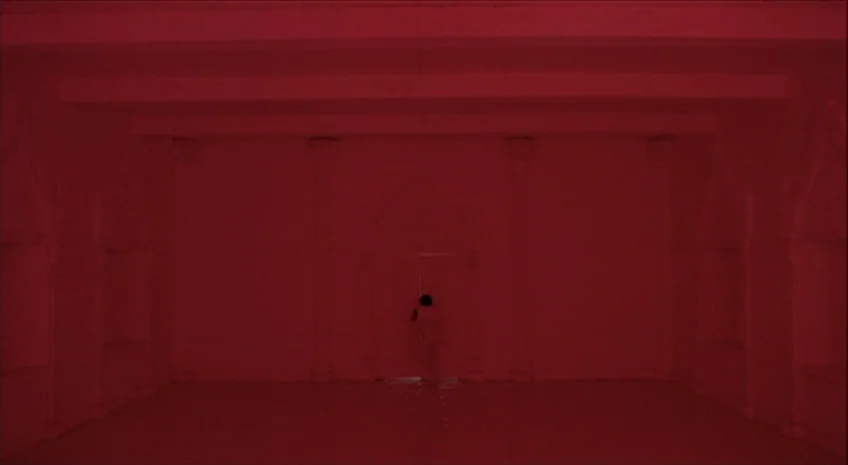 Boxer’s Omen (Mo) (1983) movie still: wide — A minimalist, empty room with symmetrical wall paneling and a central door. A solitary figure stands…