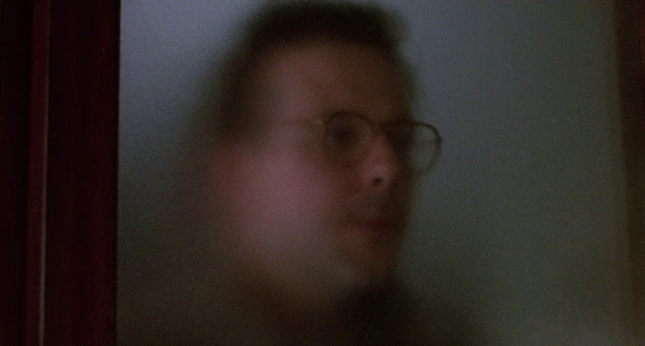Angel Heart (1987) movie still: closeup — A man's face is partially obscured behind a pane of textured frosted glass. The subject stares toward the…