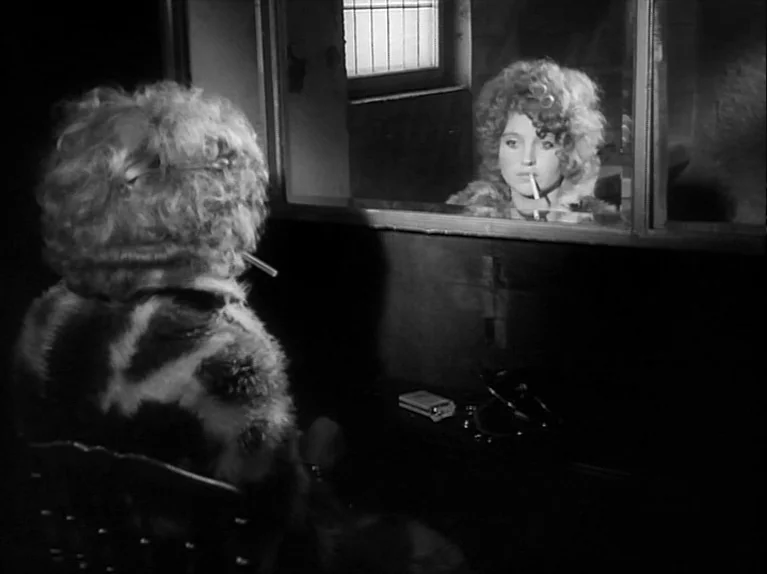 Gods Of The Plague (1970) movie still: medium — A woman sits before a mirror in a dimly lit dressing room environment. Her reflection shows her…