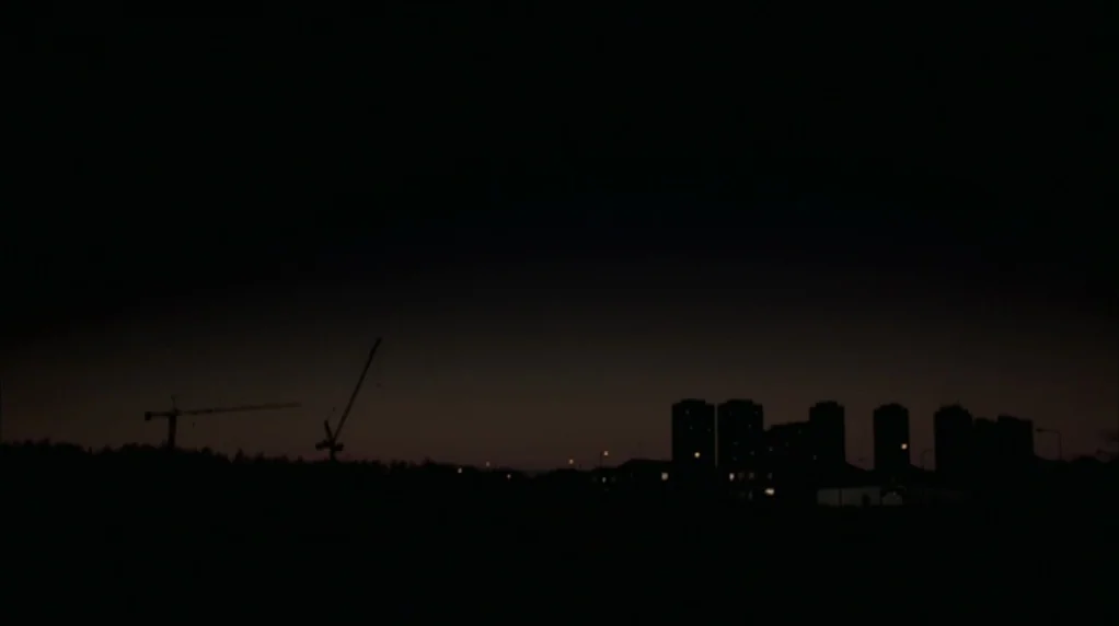 Red Road (2006) movie still: wide — A dark urban silhouette features apartment towers and construction cranes against a deep twilight sky. The…