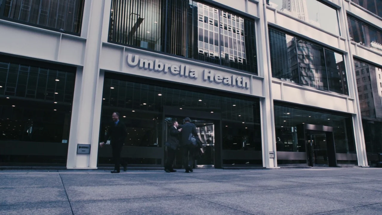 Saw VI movie still: wide — A modern glass-and-steel building facade features large silver lettering reading Umbrella Health above entrance. Three…