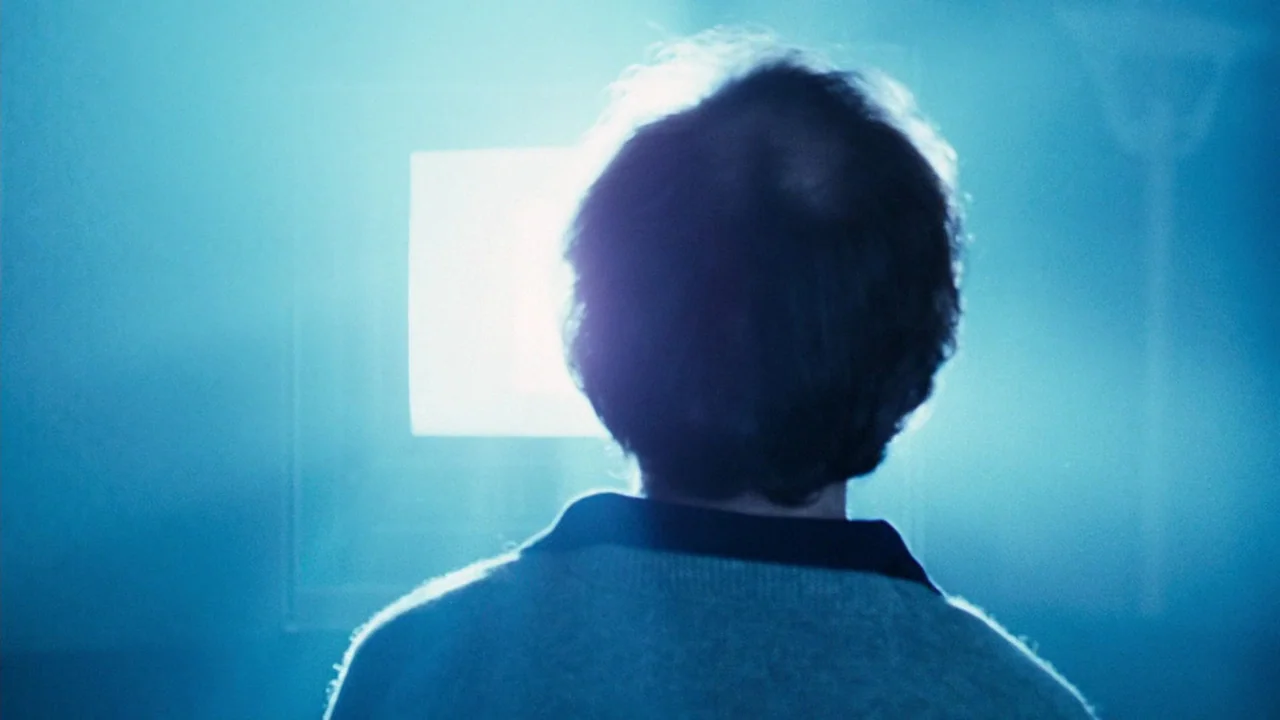 Altered States (1980) movie still: closeup — A dark, dimly lit room is illuminated solely by the glow of a screen. A man stands facing the bright…
