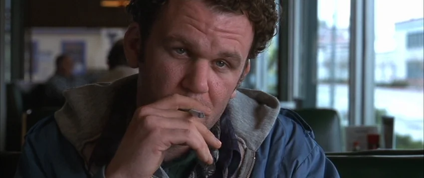 Hard Eight (1996) movie still: closeup — A man sits at a booth in a diner during the daylight hours. He holds a cigarette near his mouth while…
