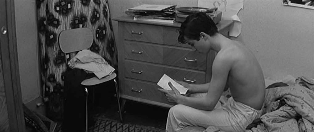Antoine and Colette (1962) movie still: medium — A spare bedroom features a wooden dresser and a simple chair against patterned wallpaper. A young…
