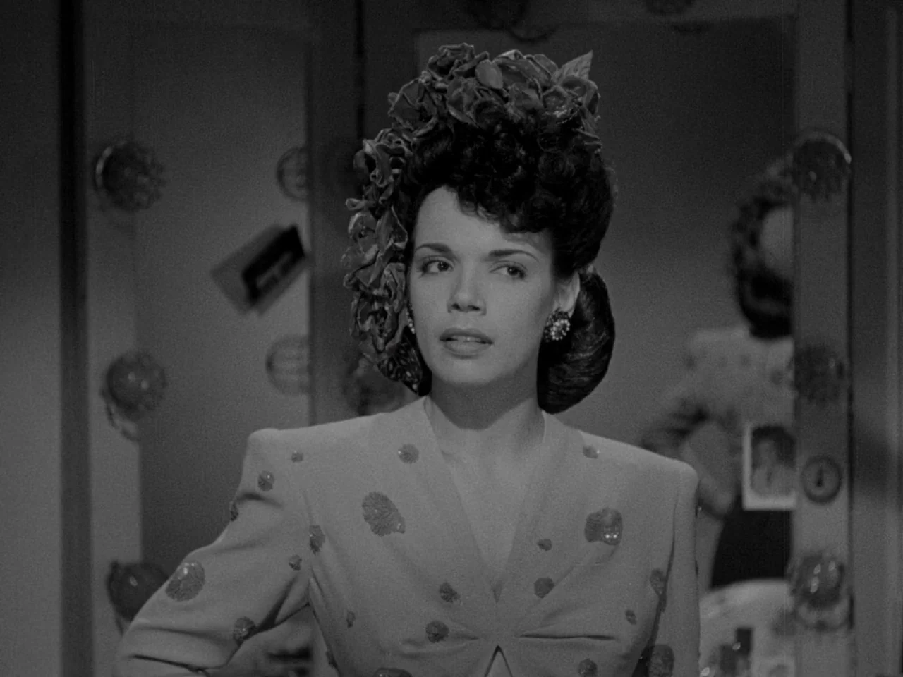 Phantom Lady (1944) movie still: medium — A dimly lit backstage area featuring a vanity mirror surrounded by circular bulbs. A woman in an elaborate…