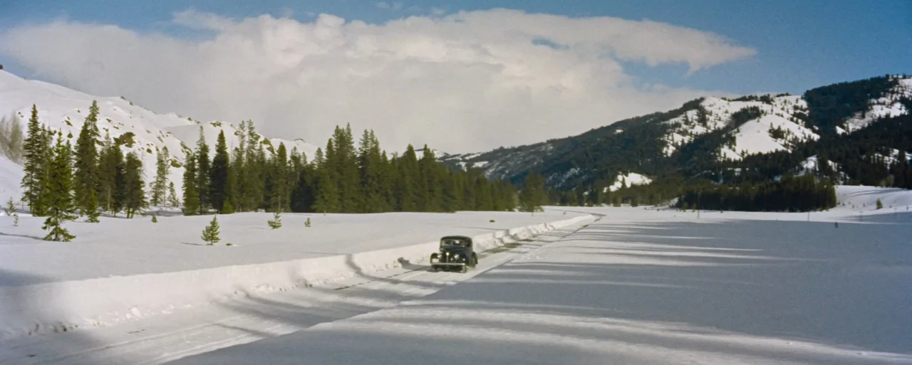 How to Marry a Millionaire movie still: wide — A dark vintage car travels down a plowed road cutting through deep snowfields. Pine forests and…