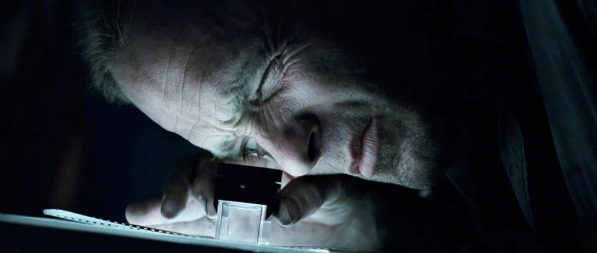 The Abyss (1989) movie still: closeup — A dark, dimly lit environment where a light table is the only illumination source. A man peers intently…