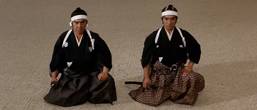 Lone Wolf and Cub: Baby Cart in Peril (1972) movie still: fullbody — Two men kneel side-by-side on a flat surface of raked sand. Both men wear…