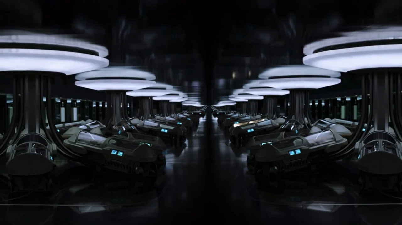 Passengers (2016) movie still: establishing — A dark, expansive room filled with numerous rows of futuristic medical stasis pods. The pods are…