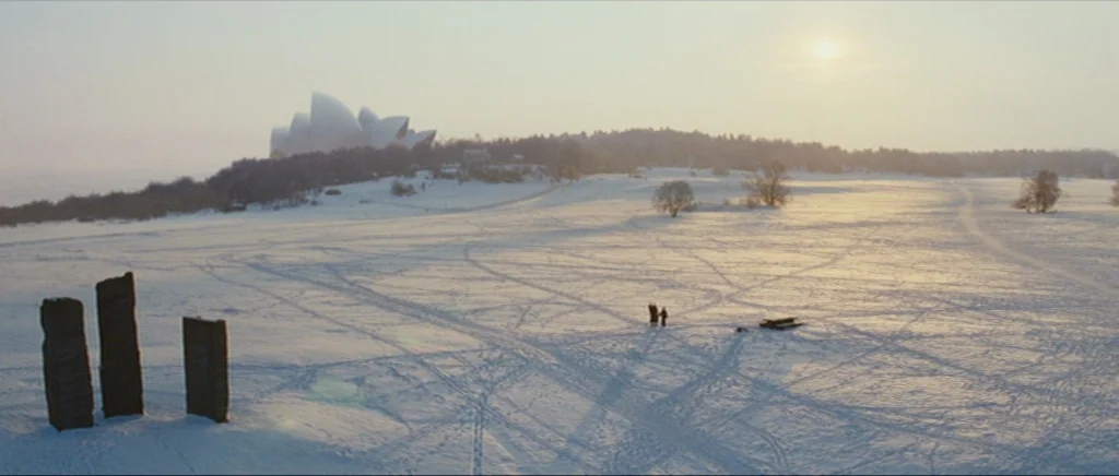 Sunshine movie still: wide — A vast, flat field covered in deep snow features three large dark vertical monoliths. In the distance, a miniature…