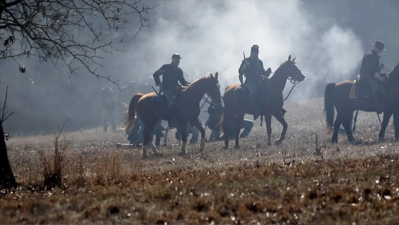 Kill Cavalry (2021) movie still: wide — A smoke-filled field during a 19th-century conflict contains several riders and dismounted soldiers.…