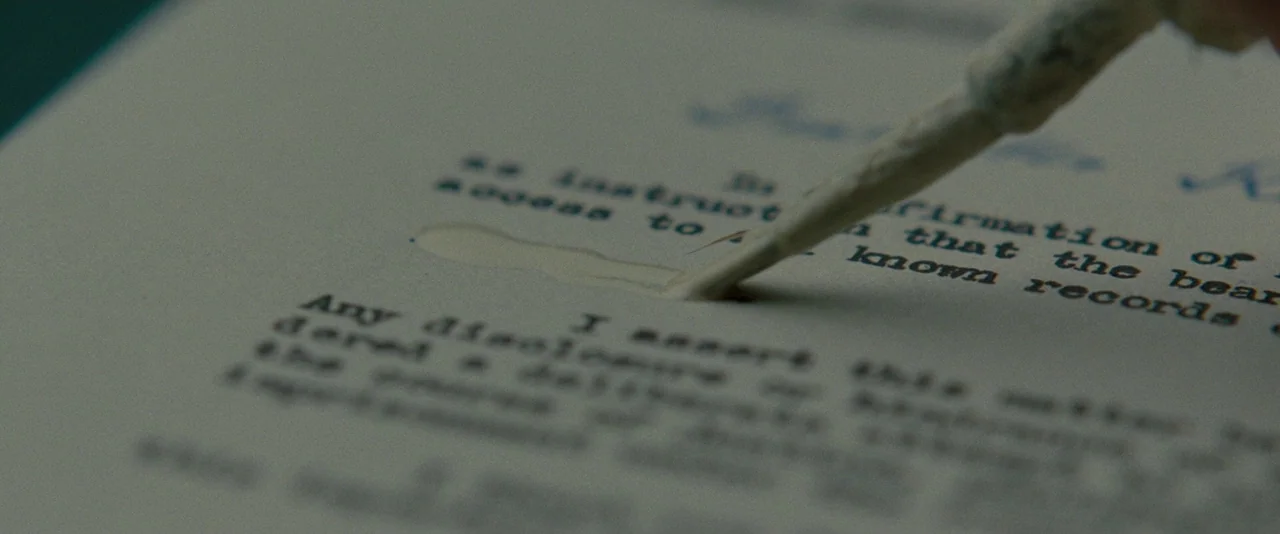 The Imitation Game (2014) movie still: closeup — A close-up view of an off-white sheet of typewritten paper on a desk. A small brush applies a…