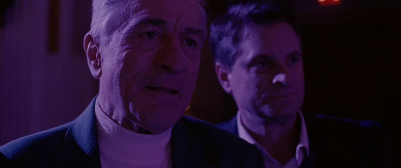 Silver Linings Playbook (2012) movie still: medium — Two men stand in a dark interior space illuminated by heavy purple lighting. The older man in…
