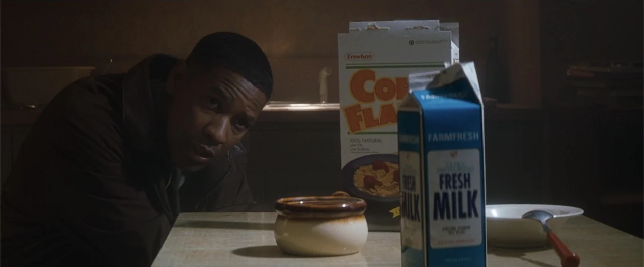 Fallen (2004) movie still: medium — A dimly lit room features a dining table with breakfast items in the foreground. A man in a leather jacket looks…