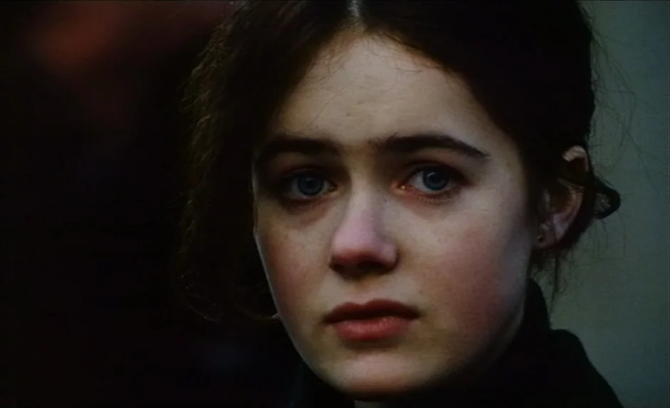 Simon, The Magician (1999) movie still: closeup — A dark indoor space with a neutral, non-descript background behind the subject. A young woman with…