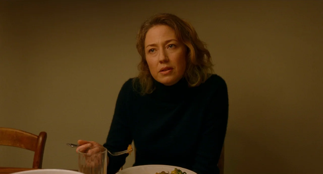 His Three Daughters (2023) movie still: medium — A woman sits at a dining table against a plain, dimly lit wall. She holds a fork while eating dinner.