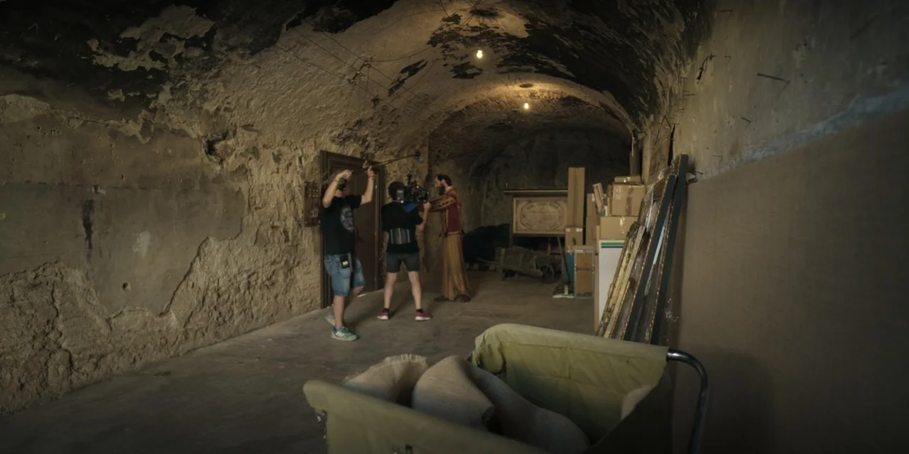The Three Wise Men: The Truth (2022) movie still: wide — An arched, rough-hewn stone cellar contains stacked cardboard boxes and a wooden cart. A…