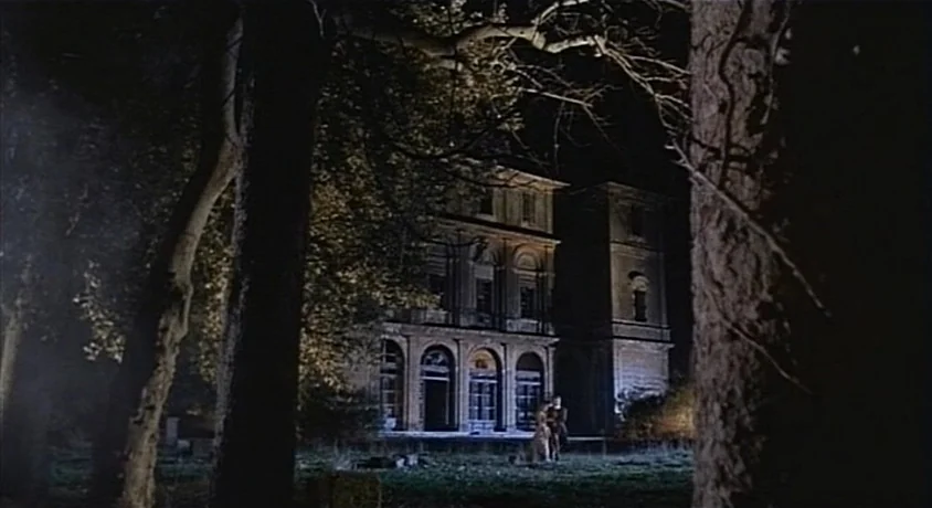 Kill, Baby Kill (1966) movie still: wide — A stone mansion with arched doorways stands framed by dark trees at night. The structure is illuminated…