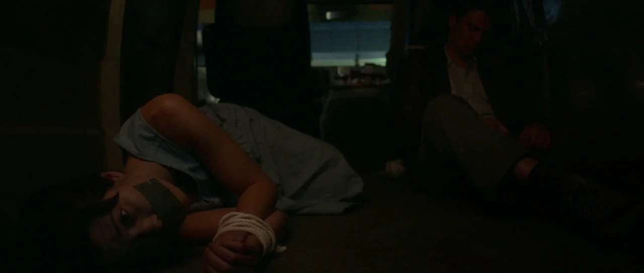 Faults (2014) movie still: medium — The interior of a dark van at night with minimal illumination coming from windows. A young woman with bound…