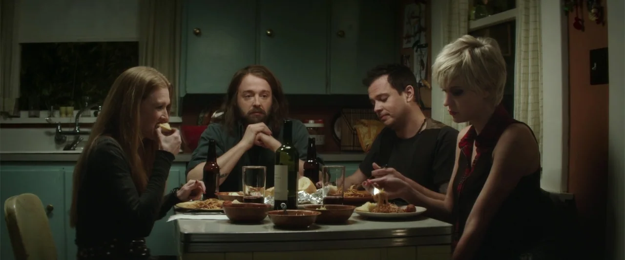 If I Stay (2014) movie still: medium — A group of four people sit around a table in a room with blue cabinets. They eat a meal of spaghetti and…