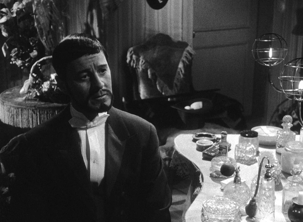 Smiles Of A Summer Night (1955) movie still: medium — A dimly lit room contains a cluttered vanity table with perfume bottles and jars. A man in a…