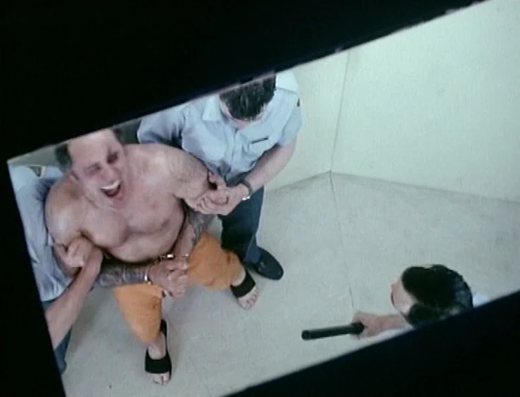 Ghosts… Of The Civil Dead (1988) movie still: fullbody — A spartan room with blank beige walls and a high angle view from above. Guards in uniforms…