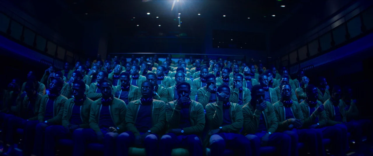 Rye Lane (2023) movie still: wide — A crowded movie theater with rows of identical men sitting in dark seats. Every man wears an identical green…