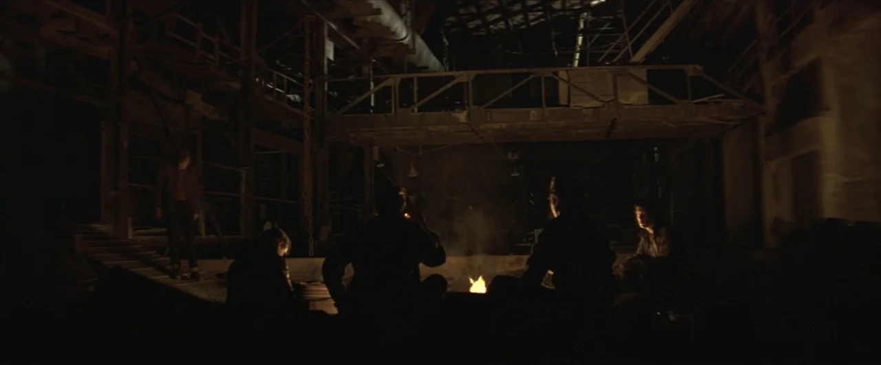 This Boy's Life (1993) movie still: wide — A dark, cavernous industrial space features exposed rafters and a large metal catwalk structure. Several…