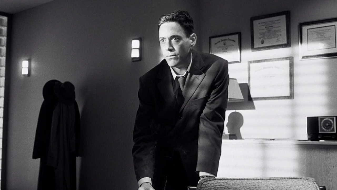 Eros (2004) movie still: medium — A professional space decorated with framed diplomas on a wall with shuttered windows. A man in a suit stands…