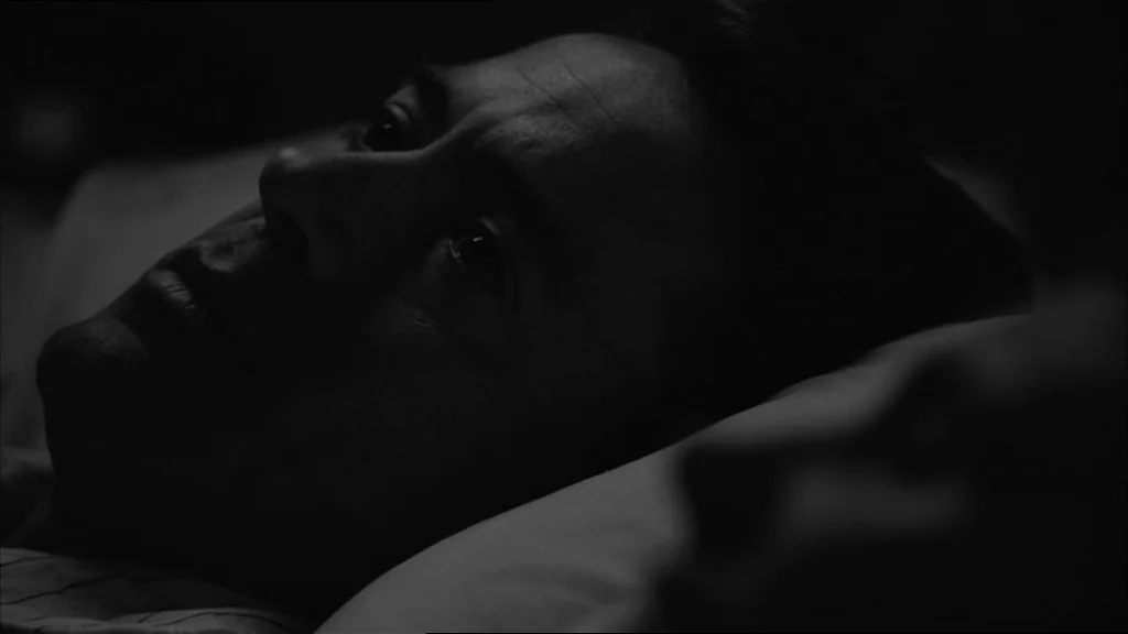 Good Night And Good Luck (2005) movie still: closeup — A dimly lit room where a man lies resting on a white pillow. He stares into the darkness…