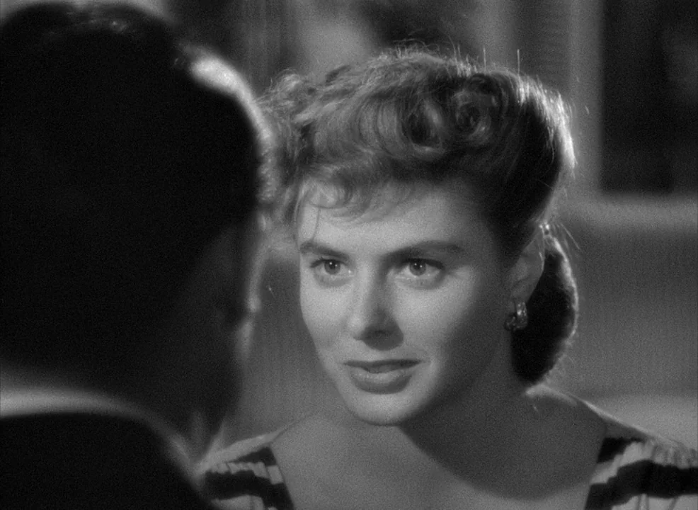 Notorious (1946) movie still: closeup — A dimly lit indoor space frames a woman from the chest up. She looks directly at someone off-screen in the…