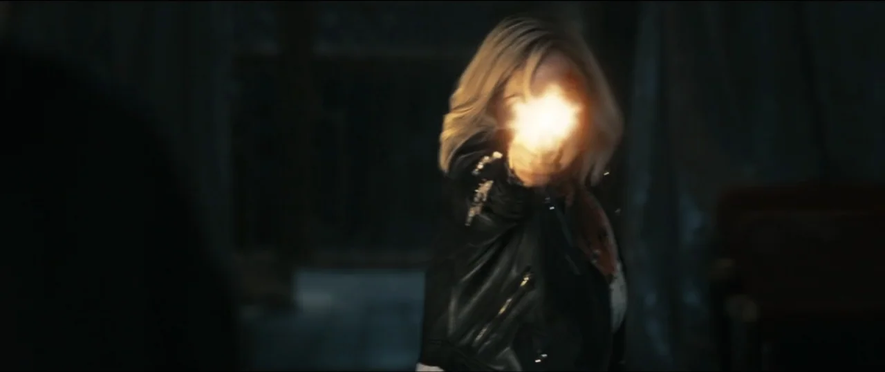 Scream VI (2023) movie still: medium — A dimly lit interior space with obscured architectural details. A woman in a leather jacket fires a pistol…