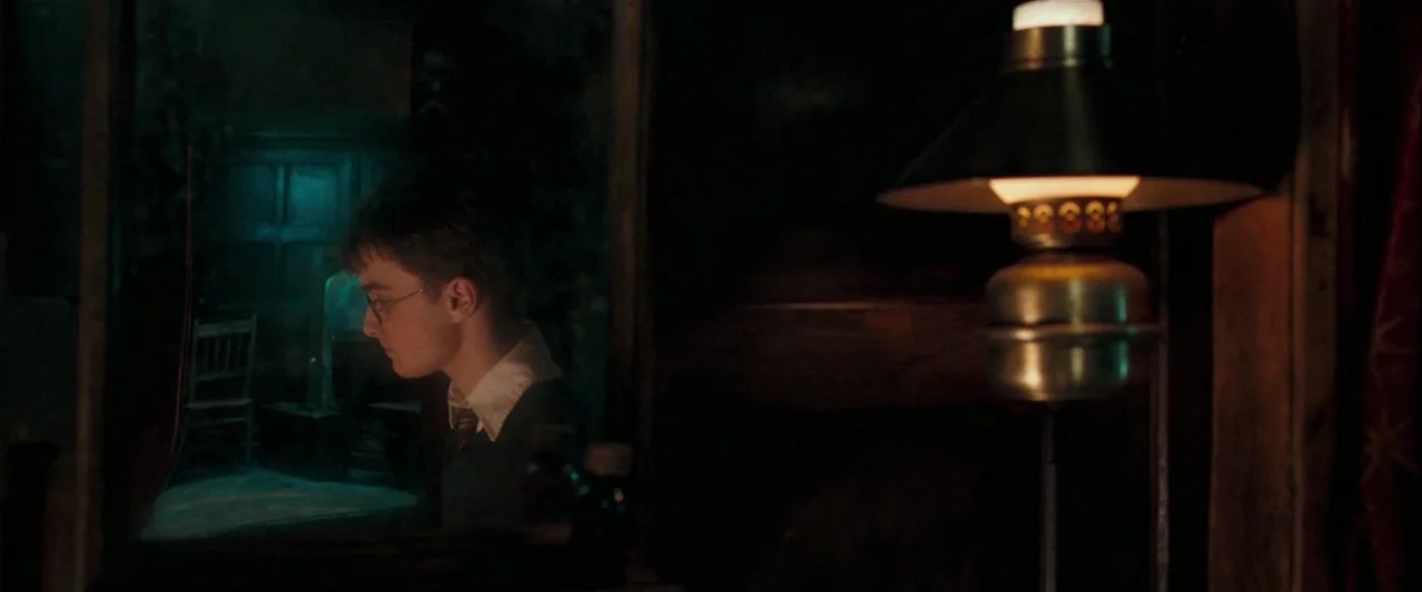 Harry Potter & The Order of the Phoenix (2007) movie still: medium — A dark, dimly lit room contains a young man reflected in a mirror. He sits at a…