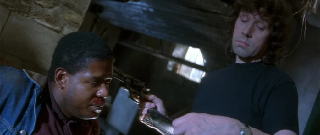 The Crying Game (1992) movie still: medium — A dimly lit unfinished basement features wooden ceiling joists and rough textured walls. A man points a…