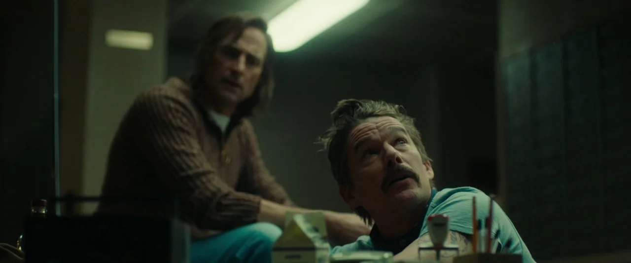 Stockholm (2019) movie still: medium — A dimly lit room with rows of dark metallic safety deposit boxes behind them. Two men in period-appropriate…