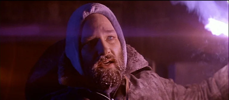 The Thing (1982) movie still: closeup — A snowy, dark arctic landscape at night with limited visibility. A bearded man with frosted facial hair…
