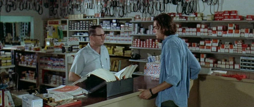 Two Lane Blacktop (1971) movie still: medium — A cluttered auto parts store has numerous shelves filled with small boxes of merchandise. An older…