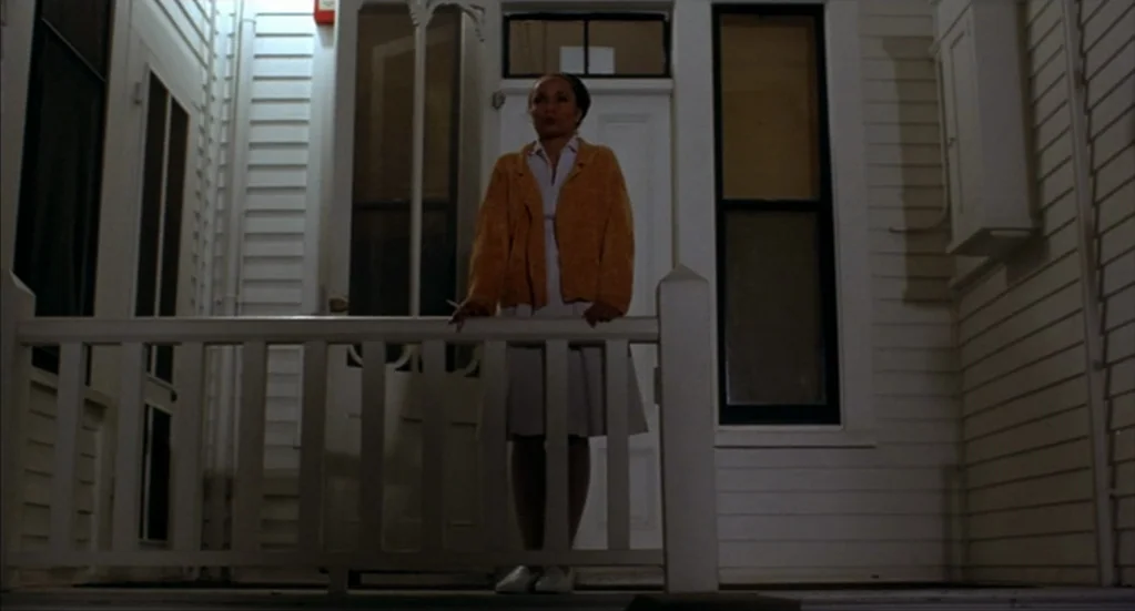 Bubba Ho-Tep (2002) movie still: fullbody — A woman stands on the white wooden porch of a classic house at night. She leans on the railing while…