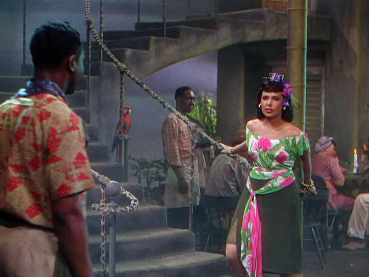 Ziegfeld Follies (1945) movie still: fullbody — A dimly lit tropical-style interior features a stone staircase and rope handrails. A woman faces a…