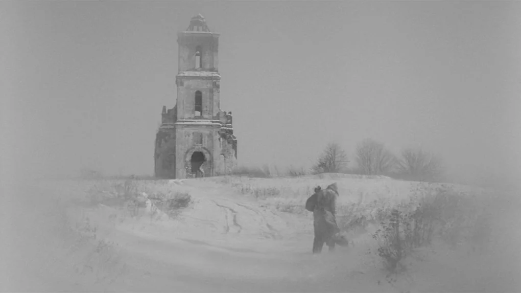 The Role (2013) movie still: wide — A desolate snow-covered landscape features a crumbling ancient stone bell tower in the distance. An elderly man…