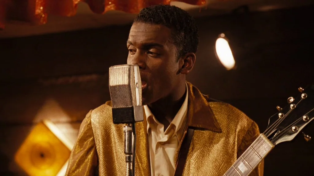 Honeydripper (2007) movie still: medium — A dimly lit club interior featuring a musician performing on a small stage. The man stands before a silver…