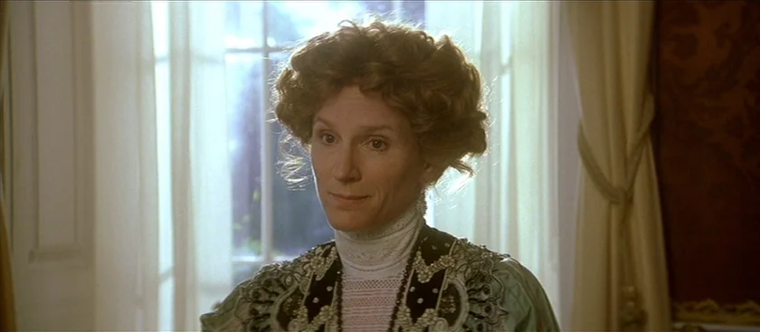 The House of Mirth (2000) movie still: closeup — An interior space features a large window with sheer curtains and dark patterned wallpaper. A woman…